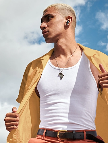 Young man with Bluetooth headphones, casual summer outfit, enjoying music outdoors.