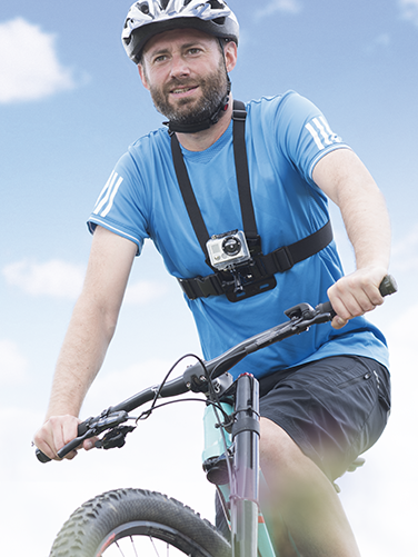 A man in a T-shirt and shorts is cycling and wearing his action camera with the Hama chest strap for GoPro