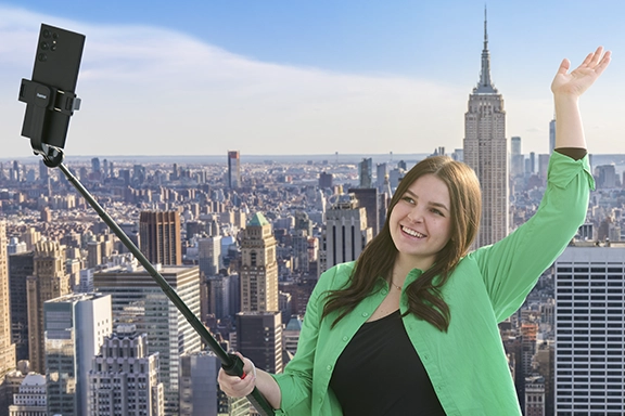 A young woman takes a selfie with the Hama selfie stick tripod “Fancy Stand 170” in front of the New York skyline